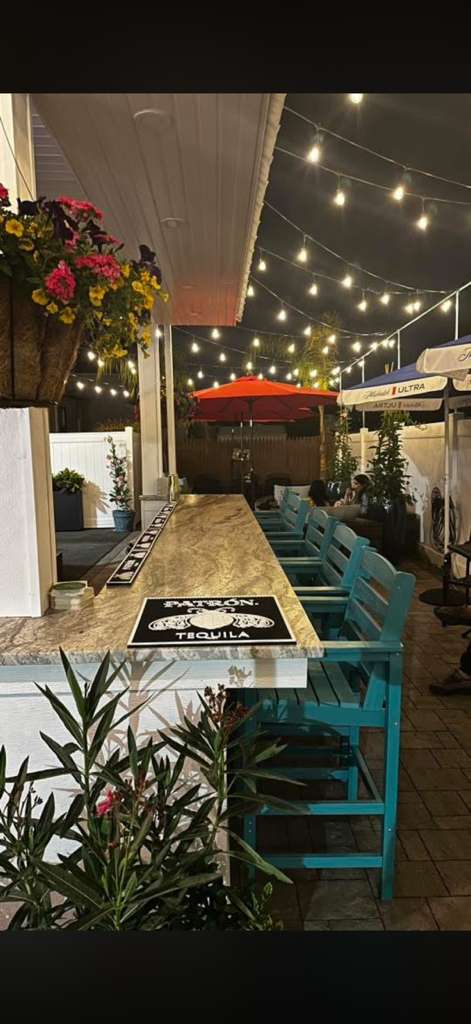 The Usual Suspects patio bar at night with string lights and Patron tequila sign