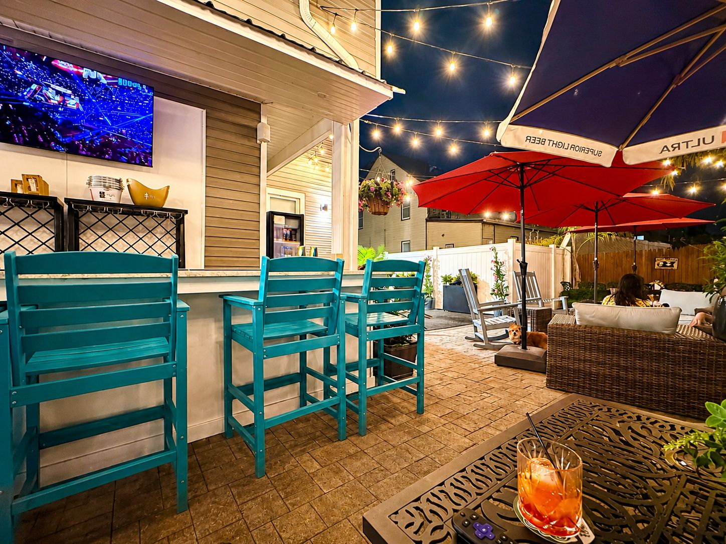 The Usual Suspects patio at night — string lights, teal bar stools, cocktail in hand