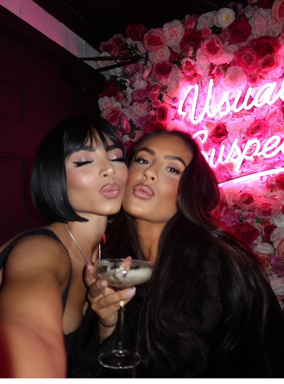 Two guests in front of the pink neon rose wall inside the bar